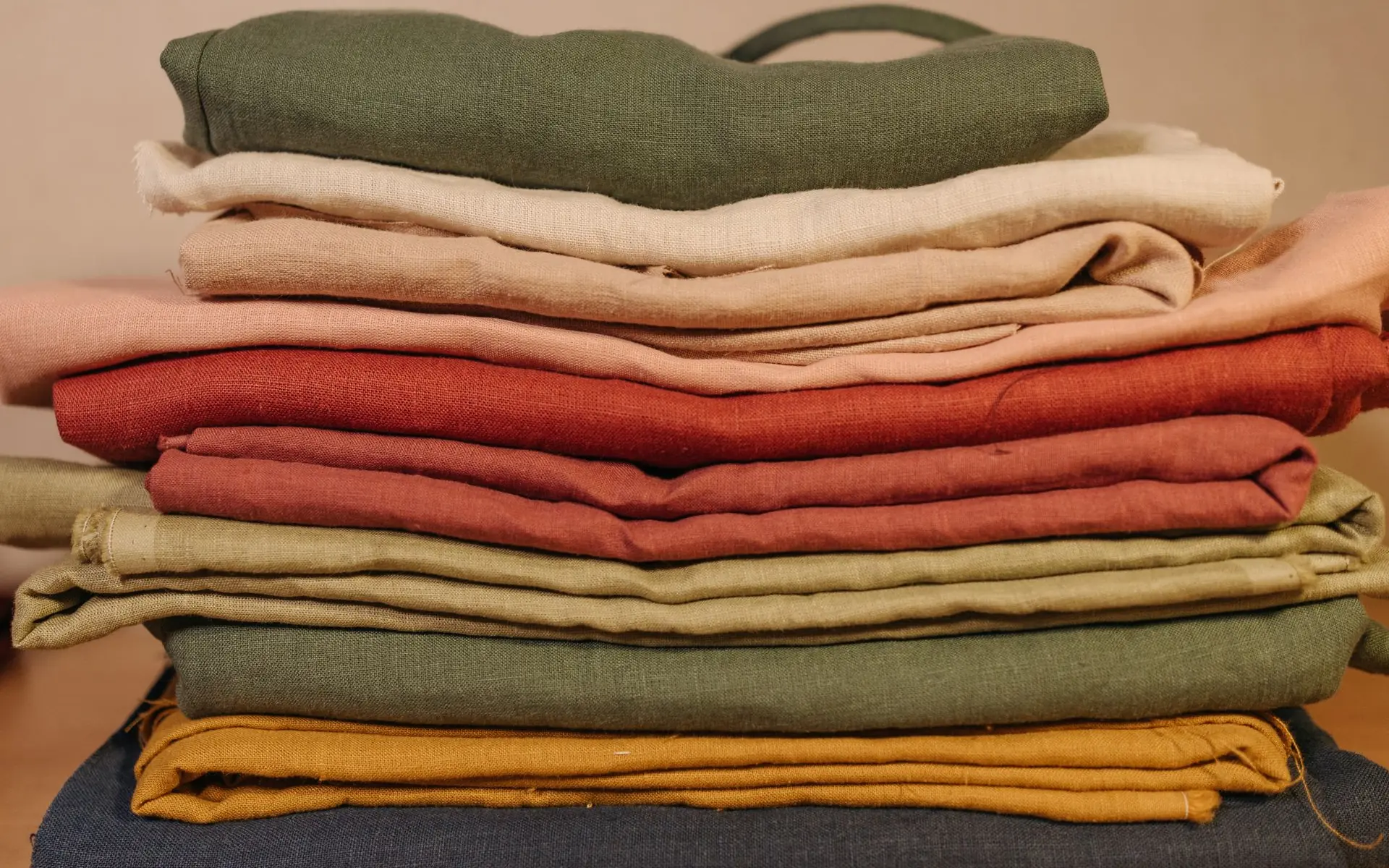 A stack of folded linen in sage green, cream, terracotta and ochre on a table